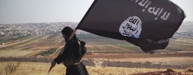 Das Bild zeigt einen Kämpfer mit der Fahne der Terrororganisation Islamischer Staat (IS).