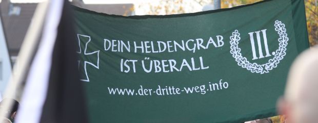 Auf dem Bild ist ein Kundgebungsbanner der Partei Der Dritte Weg mit der Aufschrift "Dein Heldengrab ist überall" zu sehen. Auf dem Bild ist ein Kundgebungsbanner der Partei Der Dritte Weg mit der Aufschrift "Dein Heldengrab ist überall" zu sehen.